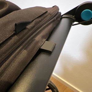 May include: Close-up of a black stroller canopy with a zipper and a black plastic clip. The canopy is attached to a black stroller frame with a blue button.