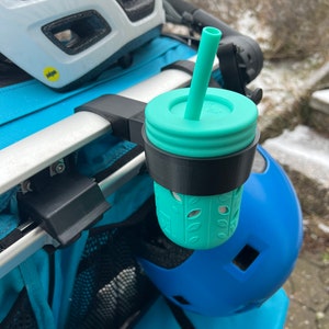 Puede incluir: Un portavasos negro y turquesa con un vaso turquesa y una pajita unidos a un cochecito.