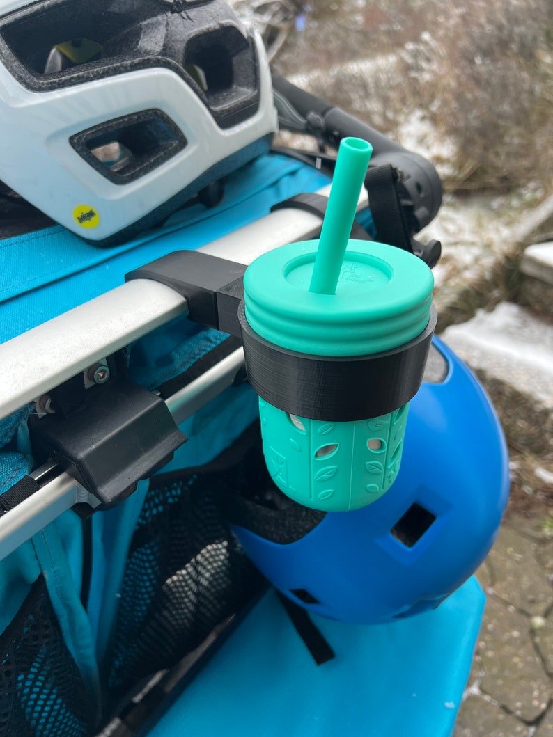 Puede incluir: Un portavasos negro y turquesa con un vaso turquesa y una pajita unidos a un cochecito.