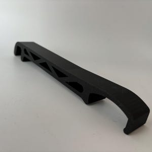 May include: A black plastic bottle opener with a unique geometric design. The opener has a curved handle and a sharp edge for opening bottles.