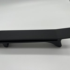 May include: A black plastic 3D printed object with a flat top and a curved bottom. The object has a slot cut into the top and two prongs on the bottom.