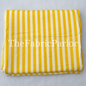 Puede incluir: Una pieza de tela doblada que presenta un patr&oacute;n repetitivo de rayas verticales amarillas y blancas. El texto TheFabricParlor est&aacute; impreso en blanco en el centro de la tela, la cual est&aacute; dispuesta en forma rectangular con bordes limpios.