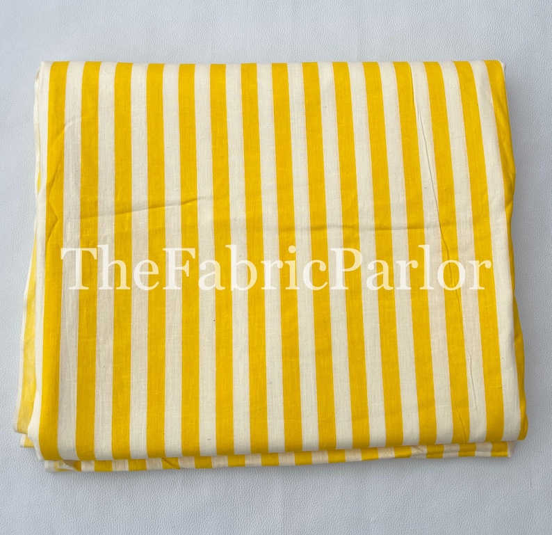 Puede incluir: Una pieza de tela doblada que presenta un patr&oacute;n repetitivo de rayas verticales amarillas y blancas. El texto TheFabricParlor est&aacute; impreso en blanco en el centro de la tela, la cual est&aacute; dispuesta en forma rectangular con bordes limpios.