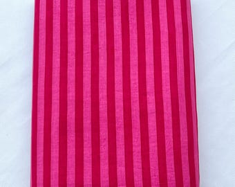 Puede incluir: Una pieza de tela rectangular que presenta un patrón vibrante de rayas verticales alternas en tonos rosa intenso y magenta. El tejido tiene una textura suave y consistente, doblado en una forma rectangular limpia, plana y uniforme.
