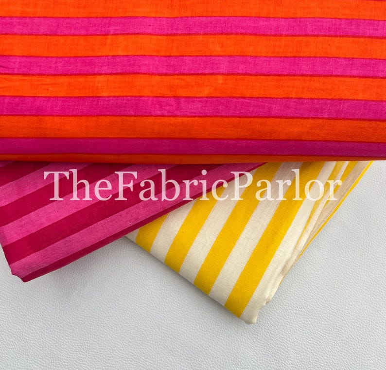 Puede incluir: Tres piezas de tela dobladas con rayas horizontales y diagonales. La tela superior tiene rayas naranjas y rosas, la del medio tiene rayas rosas y magenta, y la inferior tiene rayas amarillas y blancas. El texto dice TheFabricParlor.