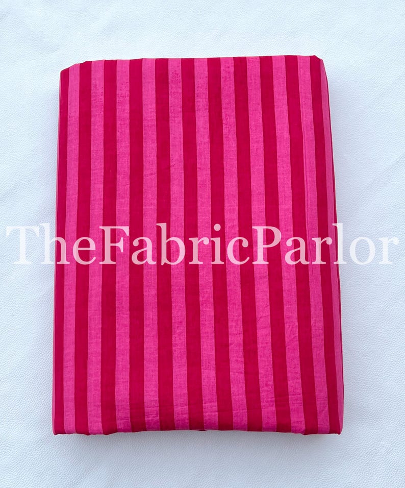 Puede incluir: Una pieza de tela doblada que presenta un patr&oacute;n de rayas verticales en tonos alternos de magenta brillante y rosa fucsia intenso. El texto TheFabricParlor est&aacute; superpuesto en blanco en el centro de la tela, que tiene una textura lisa.