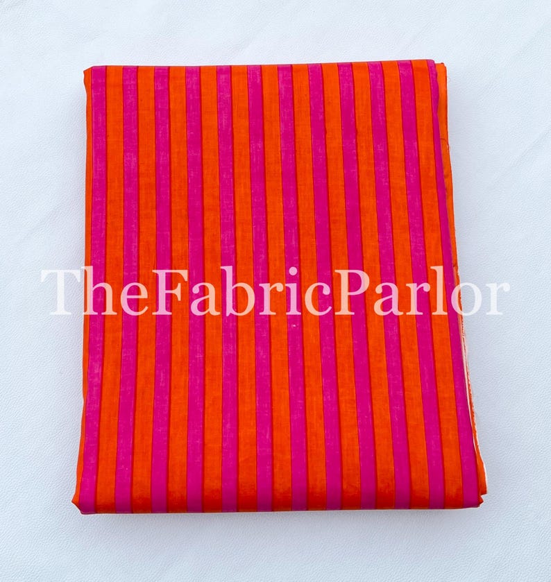Puede incluir: Una pieza de tela doblada que presenta un vibrante patr&oacute;n de rayas verticales en colores naranja brillante y rosa intenso alternados. El texto TheFabricParlor est&aacute; superpuesto en blanco sobre el centro de la tela, que est&aacute; apilada.