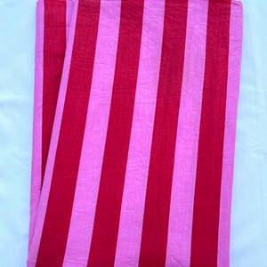 May include: A folded piece of fabric featuring a repeating vertical stripe pattern in alternating shades of bright pink and deep red. The textile has a matte finish and a visible woven texture, displayed in a clean, rectangular orientation.