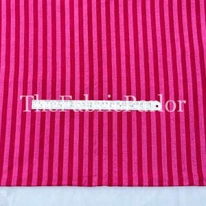 Puede incluir: Una tela con rayas verticales alternas en dos tonos de rosa. Una regla met&aacute;lica est&aacute; colocada horizontalmente en el centro, mostrando medidas en pulgadas y cent&iacute;metros, con el texto The Fabric Parlor superpuesto.