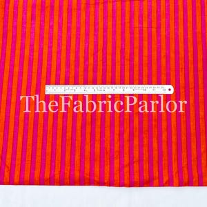 Puede incluir: Una tela con rayas verticales que alternan entre naranja brillante y rosa intenso. Una regla est&aacute; colocada horizontalmente en el centro, mostrando medidas de hasta 30 cm. El texto TheFabricParlor est&aacute; superpuesto en blanco en el medio.