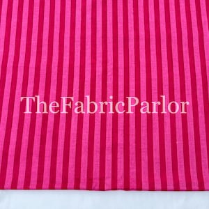 Puede incluir: Una tela textil con un patr&oacute;n repetitivo de rayas verticales en tonos alternos de rosa brillante y magenta intenso. El texto TheFabricParlor est&aacute; superpuesto en blanco en el centro de la superficie de la tela a rayas.