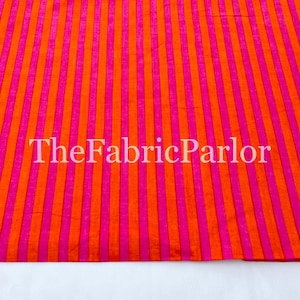 Puede incluir: Una tela textil con un patr&oacute;n de rayas verticales repetitivas en naranja vibrante y rosa brillante. La superficie tiene una textura tejida sutil. El texto TheFabricParlor est&aacute; superpuesto en blanco sobre el dise&ntilde;o de la tela a rayas.