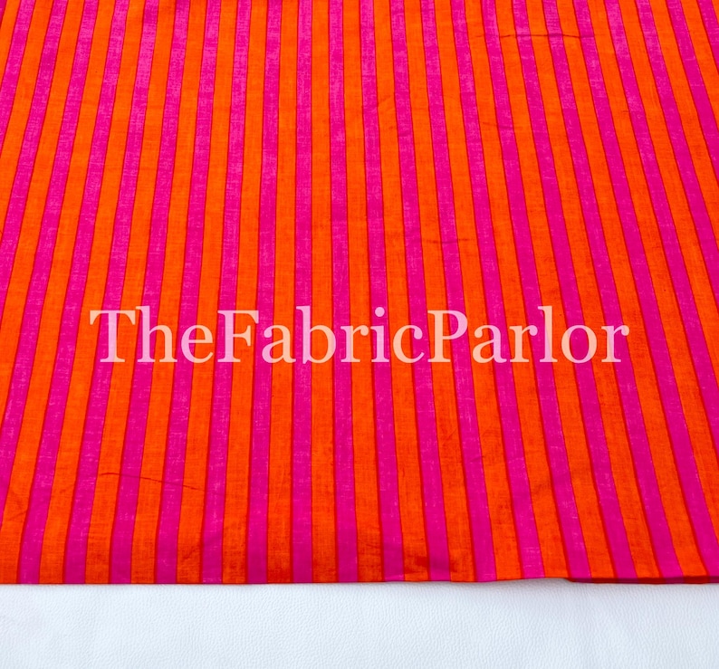 Puede incluir: Una tela textil con un patr&oacute;n de rayas verticales repetitivas en naranja vibrante y rosa brillante. La superficie tiene una textura tejida sutil. El texto TheFabricParlor est&aacute; superpuesto en blanco sobre el dise&ntilde;o de la tela a rayas.