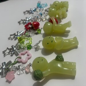 Peut inclure: Une collection de porte-cl&eacute;s faits &agrave; la main avec divers breloques. Les porte-cl&eacute;s pr&eacute;sentent des cha&icirc;nes argent&eacute;es et une vari&eacute;t&eacute; de breloques, notamment des croix, des &eacute;toiles, des fleurs et de petites figurines vert clair. Certaines breloques sont roses, rouges et transparentes.