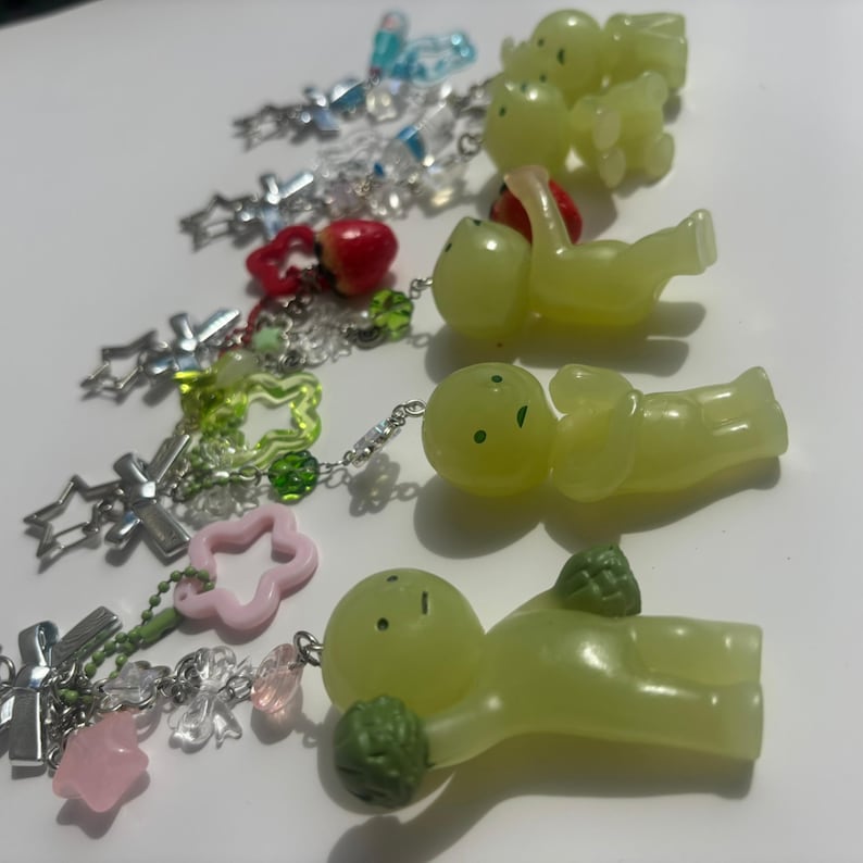 Peut inclure: Une collection de porte-cl&eacute;s faits &agrave; la main avec divers breloques. Les porte-cl&eacute;s pr&eacute;sentent des cha&icirc;nes argent&eacute;es et une vari&eacute;t&eacute; de breloques, notamment des croix, des &eacute;toiles, des fleurs et de petites figurines vert clair. Certaines breloques sont roses, rouges et transparentes.