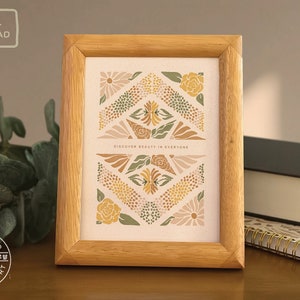 May include: A framed print with a geometric design featuring flowers in shades of green, yellow, and brown. The print has the text "Discover beauty in everyone" in the center.