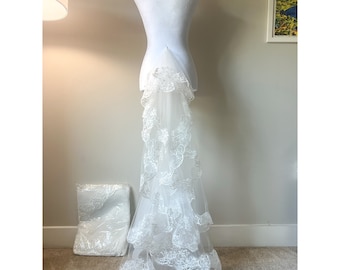 May include: A white bridal veil with a layered, scalloped lace design. The veil is displayed on a white dress form.