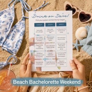 Op de afbeelding: Een vrijgezellenfeestspel met de tekst "Drink or Dare!" op een zandstrand. De spelkaart bevat uitdagingen. Een blauwe bikini top met bloemenprint, zonnebril en een cocktail zijn ook zichtbaar.