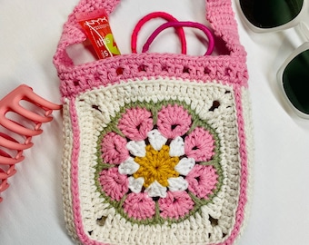 May include: A pink crocheted bag with a white and pink flower design. The bag has a pink strap and is filled with hair ties and lip gloss.