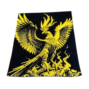 May include: A black and yellow knitted scarf with a phoenix design. The phoenix is depicted with its wings spread wide and flames surrounding it.