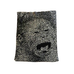 May include: A black and white textile with a pixelated image of a screaming face. The image is a close-up of a face with an open mouth, eyes, and ears. The textile has a rectangular shape.