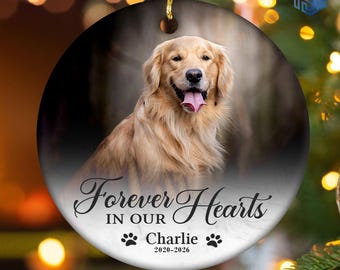 May include: A round ceramic ornament featuring a golden retriever with its tongue out. The text reads Forever In Our Hearts, the name Charlie, and the years 2020-2026, accompanied by two black paw print icons. It includes a gold hanging loop.