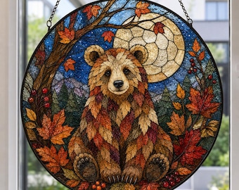 Könnte beinhalten: Ein runder Buntglas-Sonnenfänger mit einem Bären aus Herbstblättern. Der Bär sitzt in einer Waldlandschaft mit einem großen Vollmond, orangefarbenen und roten Ahornblättern sowie kleinen roten Beeren, eingefasst in einen dunklen Metallrahmen.