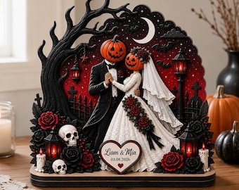 Könnte beinhalten: Eine dekorative Tischfigur mit einem Brautpaar mit Kürbisköpfen in festlicher Hochzeitskleidung. Die Szene zeigt einen schwarzen Baum, rote Rosen, Totenköpfe, Laternen und ein herzförmiges Schild mit der Aufschrift Liam & Mia 03.08.2026.