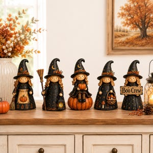 May include: Five decorative witch figurines wearing black pointed hats with gold stars and moons. Each figure has blonde hair and a black dress. They hold items including a broom, a lantern, a pumpkin, a basket of mushrooms, and a sign reading Boo Crew.
