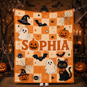 May include: A rectangular fleece blanket featuring an orange and cream checkered pattern with Halloween motifs including ghosts, bats, spiders, spiderwebs, pumpkins, and stars. The name SOPHIA is printed in large orange letters across the center.