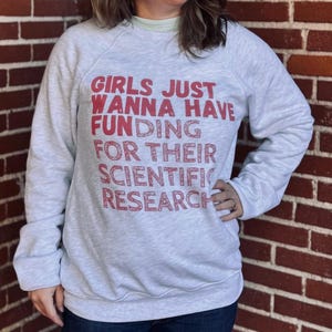May include: A gray sweatshirt with the text "Girls Just Wanna Have Funding For Their Scientific Research" printed in red.