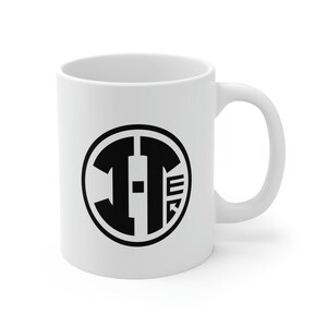 May include: White ceramic mug with a black circle design featuring the letters "I-T" in a bold, geometric font.