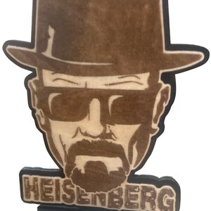 May include: A wooden cutout of Walter White, a character from the TV show Breaking Bad, wearing a brown hat and sunglasses. The cutout has the word "HEISENBERG" written below it.