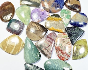 May include: A collection of polished gemstones in various shapes and colors, including oval, teardrop, and rectangular forms. The stones display a range of hues, such as green, purple, brown, and blue, with unique patterns and textures. The gemstones are displayed on a white surface.