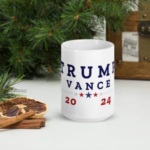 May include: White ceramic coffee mug with a blue and red design. The mug features the text "TRUMP VANCE 20** 24" with three red stars and three blue stars.