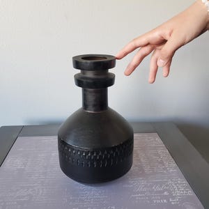 May include: A black ceramic vase with a textured design and a wide, round opening. The vase has a unique, modern style.