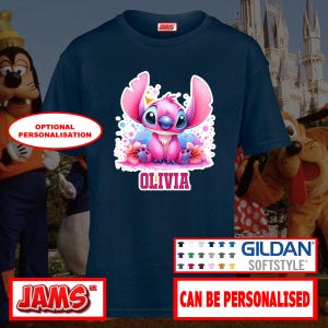 May include: Navy blue Gildan Softstyle t-shirt featuring a colorful graphic of a pink cartoon character with the name "Olivia". The shirt has a crew neck and short sleeves. The text "Can Be Personalised" is also visible.