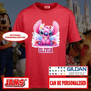 May include: Red t-shirt featuring a pink cartoon character with large ears, blue eyes, and the name "Olivia" in white. The shirt has a crew neck and short sleeves. The Gildan Softstyle brand is visible.