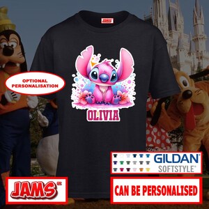 May include: Black t-shirt featuring a pink cartoon character with the name "OLIVIA" in pink letters. The character has large ears and is surrounded by colorful accents. The shirt is from Gildan Softstyle and can be personalized.
