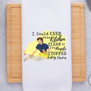 May include: White kitchen towel with a retro-style illustration of a woman cleaning a sink. The text reads "I could keep this kitchen clean if you people stopped eating here."
