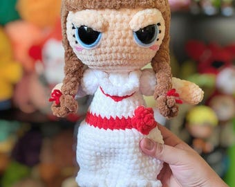 May include: A handmade crochet doll with a white dress and red accents. The doll has brown hair in braids, large blue eyes, and a slightly grumpy expression. The doll is approximately 8 inches tall.