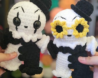 May include: Two handmade crochet plush dolls featuring black and white yarn. The left doll has black eye makeup and a black top hat. The right doll wears yellow sunflower-shaped glasses and a black top hat. Both dolls have ruffled collars.