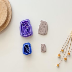 May include: Four cookie cutters in different sizes, two are purple and two are gray. The cutters are shaped like bags of coffee beans.