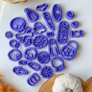 May include: A set of 20 purple plastic Halloween cookie cutters featuring various spooky designs, including ghosts, pumpkins, skulls, bats, spiders, and candy.