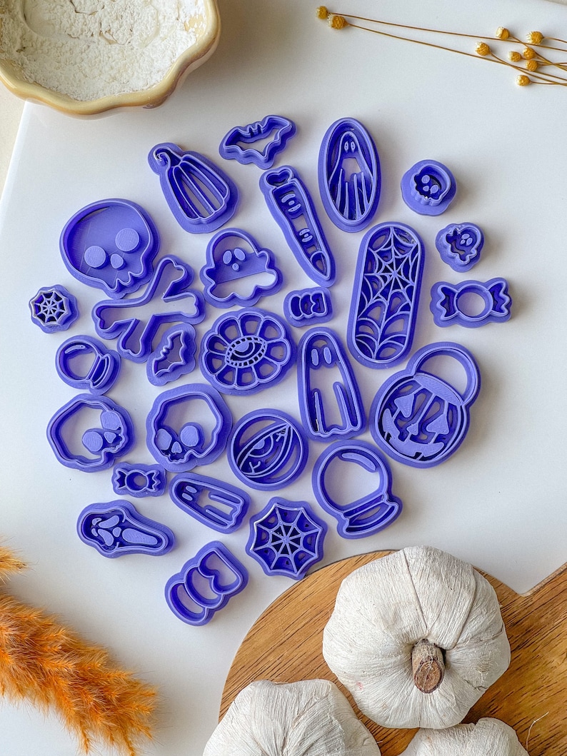 May include: A set of 20 purple plastic Halloween cookie cutters featuring various spooky designs, including ghosts, pumpkins, skulls, bats, spiders, and candy.