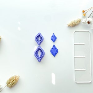May include: A set of four purple plastic cookie cutters in the shape of a teardrop. Two of the cutters are layered to create a larger teardrop shape.