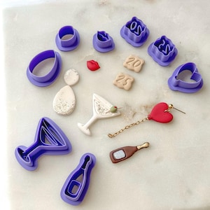 May include: A set of purple plastic cookie cutters in various shapes, including a martini glass, a champagne bottle, a heart, lips, and numbers 20 and 25. There are also small clay decorations, including a martini glass, a champagne bottle, a heart, and numbers 20 and 25.