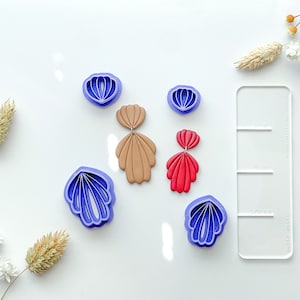 May include: A set of six purple polymer clay cutters shaped like seashells, with two brown and two red polymer clay earrings. The earrings are shaped like seashells and are layered.