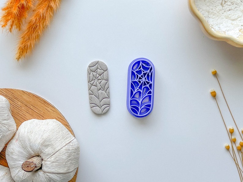 May include: Two cookie cutters, one gray and one blue, shaped like a spider web. The cutters are on a white surface.