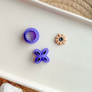 Könnte beinhalten: Drei violette Plastik-Ausstecher in Form einer Blume, eines vierblättrigen Kleeblatts und eines Kreises mit gewellten Rändern. Die Ausstecher befinden sich auf einer weißen Oberfläche.